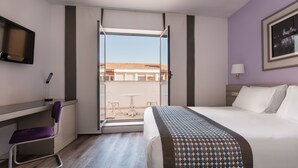 A hotel room with a bed, a desk, a chair, a TV, and a window with a view of buildings. - Exe Salamanca (Salamanca)