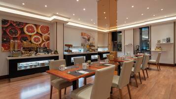 Un comedor moderno con una larga mesa de madera, sillas acolchadas y una cocina al fondo.