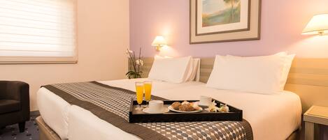 Una habitación de hotel con dos camas, una mesa de comedor con alimentos para el desayuno y un cuadro en la pared.