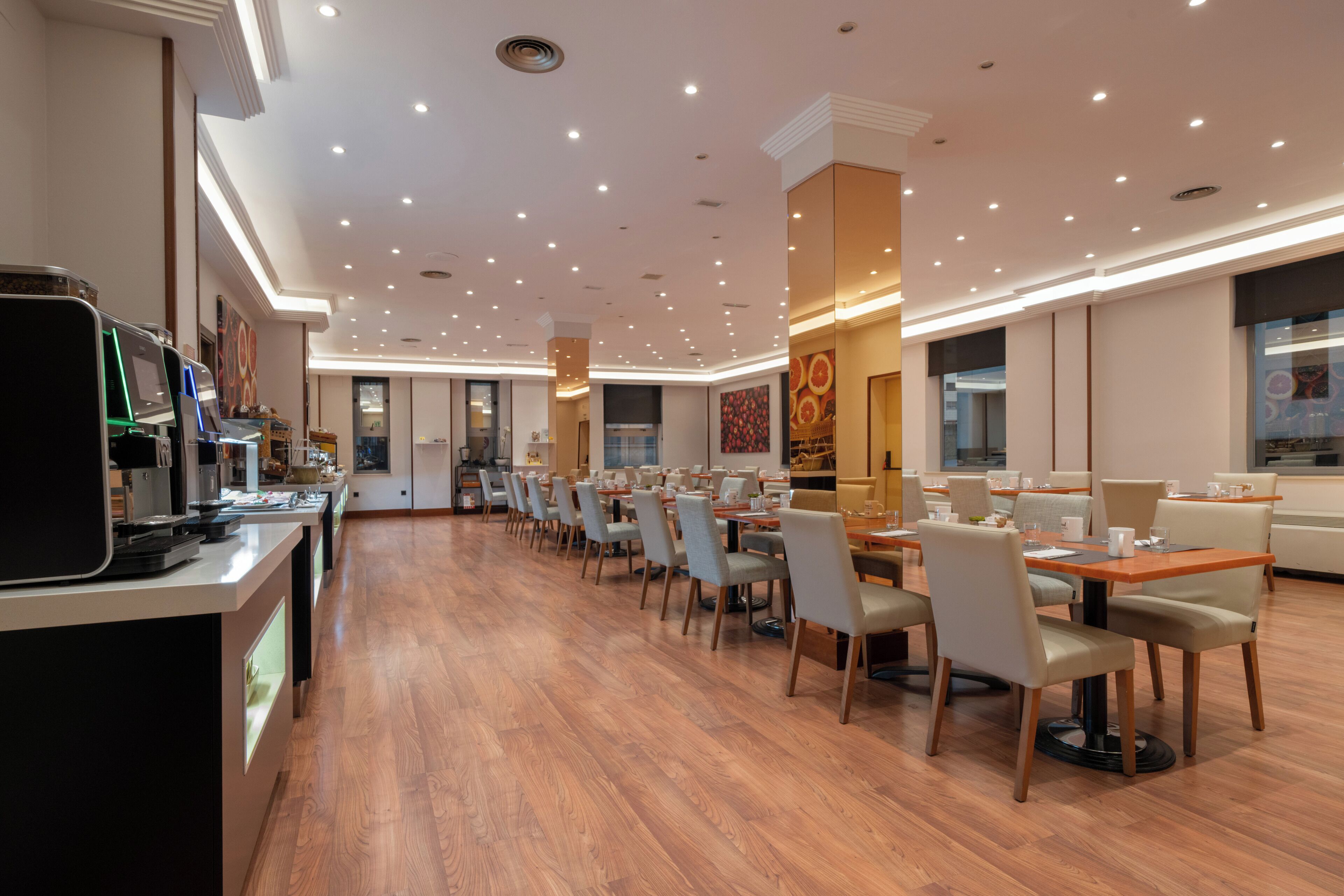 Un comedor amplio con suelo de madera, varias mesas y sillas, y un diseño de techo moderno con iluminación empotrada.