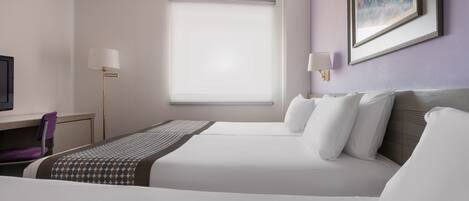 A hotel room with two beds, a desk, a chair, a window with blinds, and a painting on the wall.