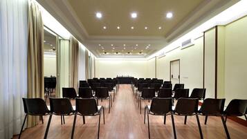A conference room with rows of chairs facing a long table, a ceiling with recessed lighting, and a plain wall with a door.