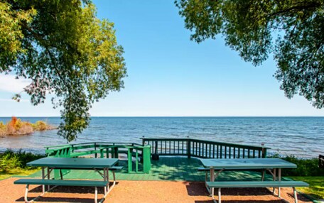 A picnic area with green benches and a wooden deck overlooking a body of water.