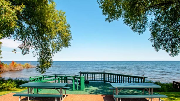 A picnic area with green benches and a wooden deck overlooking a body of water.
