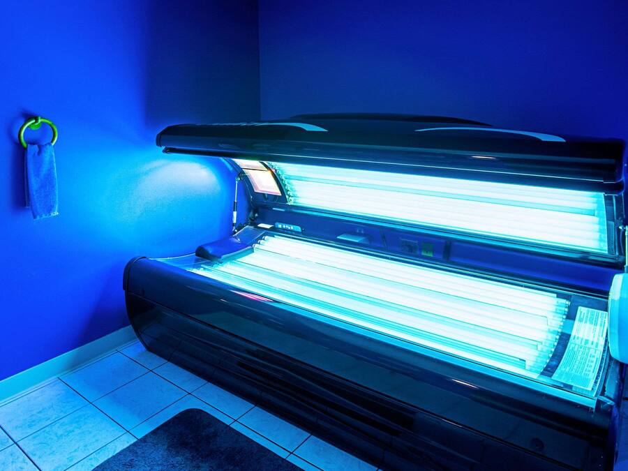 Una cama bronceadora en una habitación con paredes azules y suelo de baldosas.