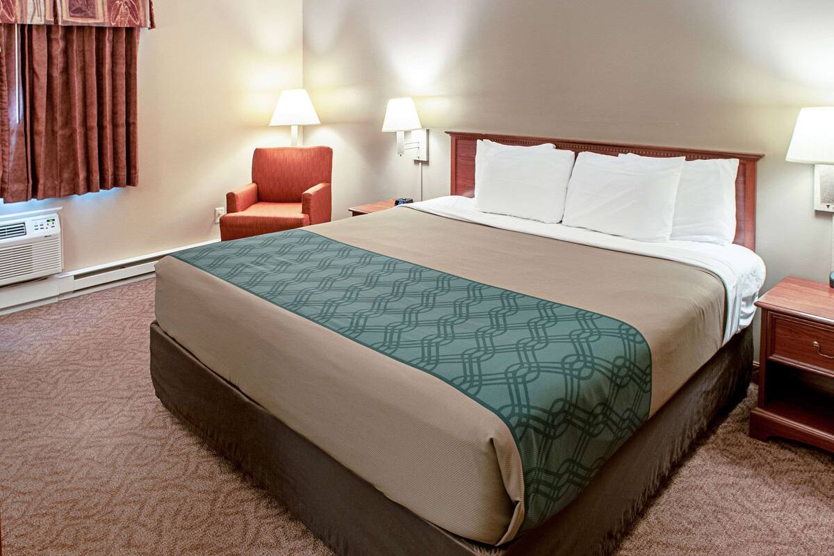 A hotel room with a large bed, two bedside lamps, a chair, and a heater.
