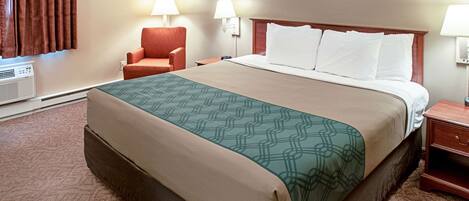 Quarto de hotel com uma cama grande, duas luminárias laterais, uma cadeira e um aquecedor.