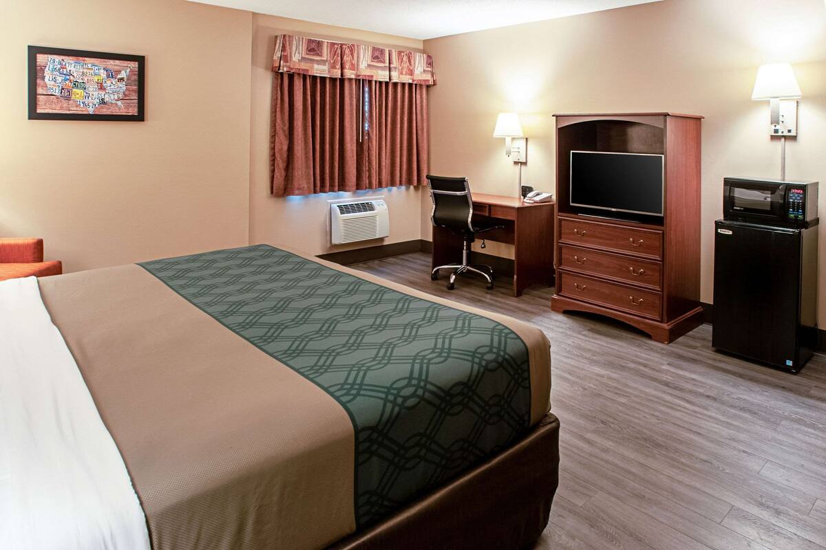 A hotel room with a bed, a desk, a chair, a television, a dresser, and a refrigerator.