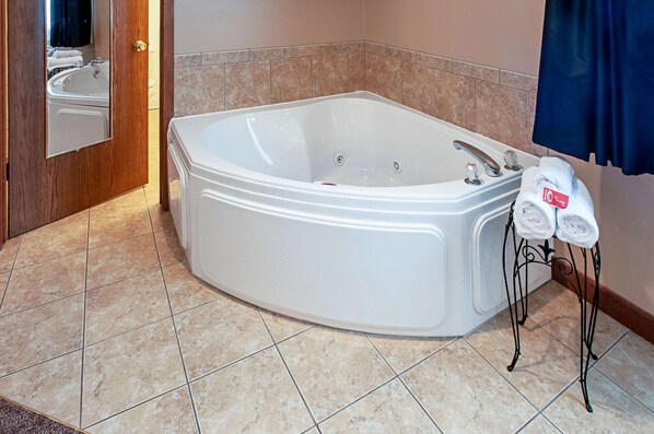 A bathroom with a large white bathtub, a wooden door, and a towel rack with two towels.