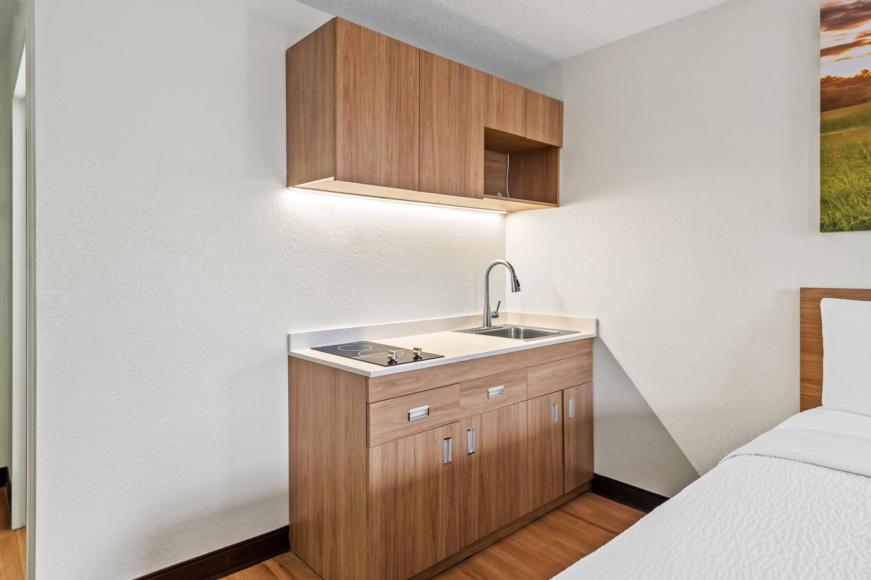 A compact kitchenette with a sink, countertop, and wooden cabinets.