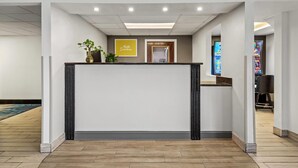 Un espace d’accueil comprenant un comptoir de réception, un panneau indiquant « Bonjour et bienvenue », une plante et un écran numérique.