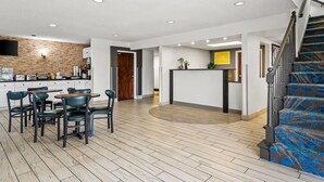 Un vaste espace de vie doté d’un plancher en bois, d’un ensemble de salle à manger, d’un coin cuisine avec un mur de crédence en briques et d’un escalier recouvert d’une moquette à motifs.