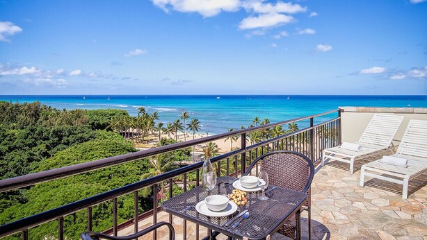 Un balcon avec une table dressée pour deux personnes, offrant une vue sur la plage et l’océan.
