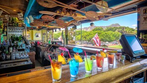 Un bar offrant une vue sur une montagne, agrémenté de plantes tropicales et décoré d’un drapeau.