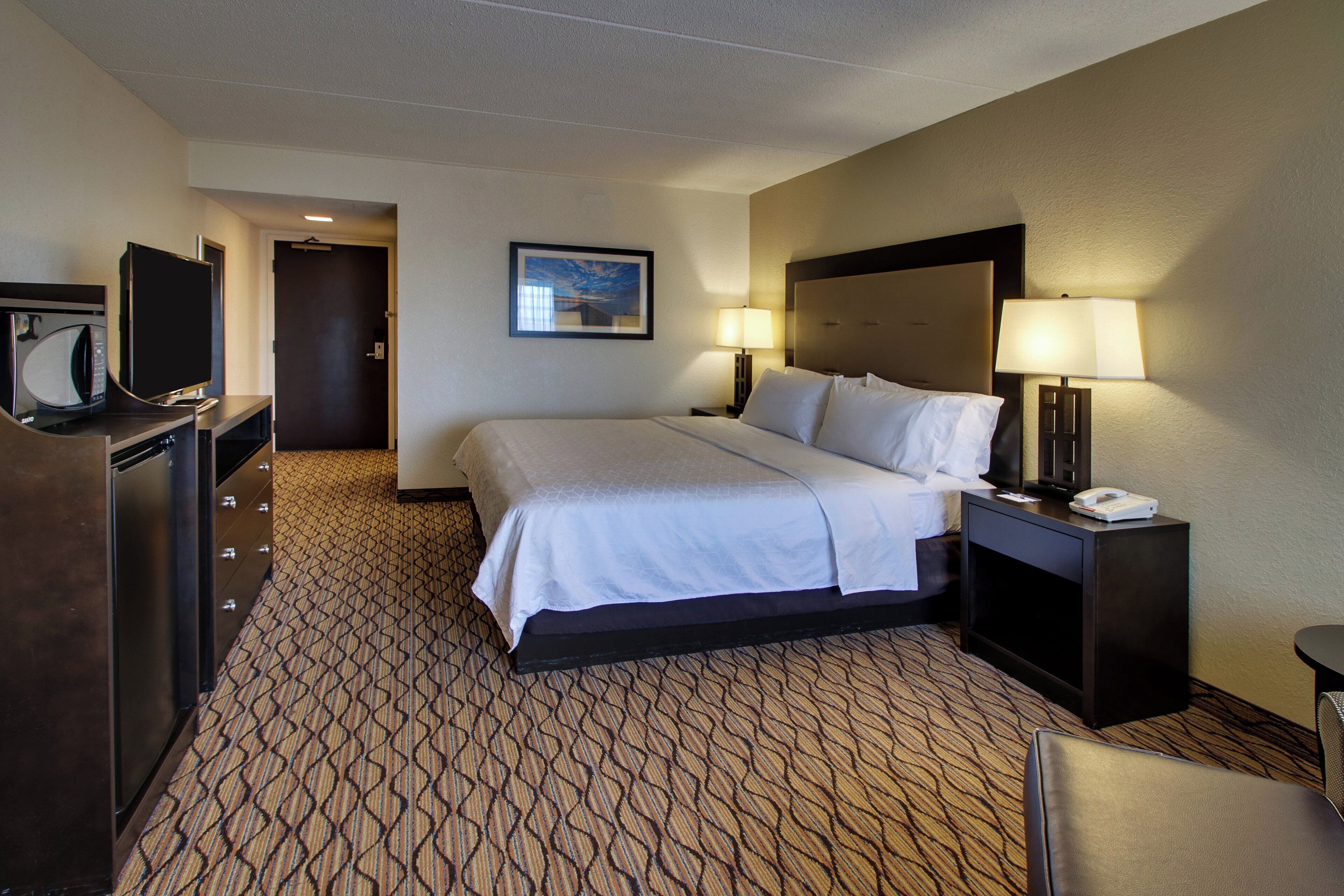 Una habitación de hotel con cama, escritorio con lámpara, televisión y puerta.