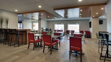 A spacious dining area with multiple tables and chairs, a bar area with stools, and a large window providing natural light.