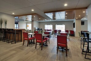A spacious dining area with multiple tables and chairs, a bar area with stools, and a large window providing natural light. - Holiday Inn Express Baltimore-BWI Airport West by IHG (Hanover)