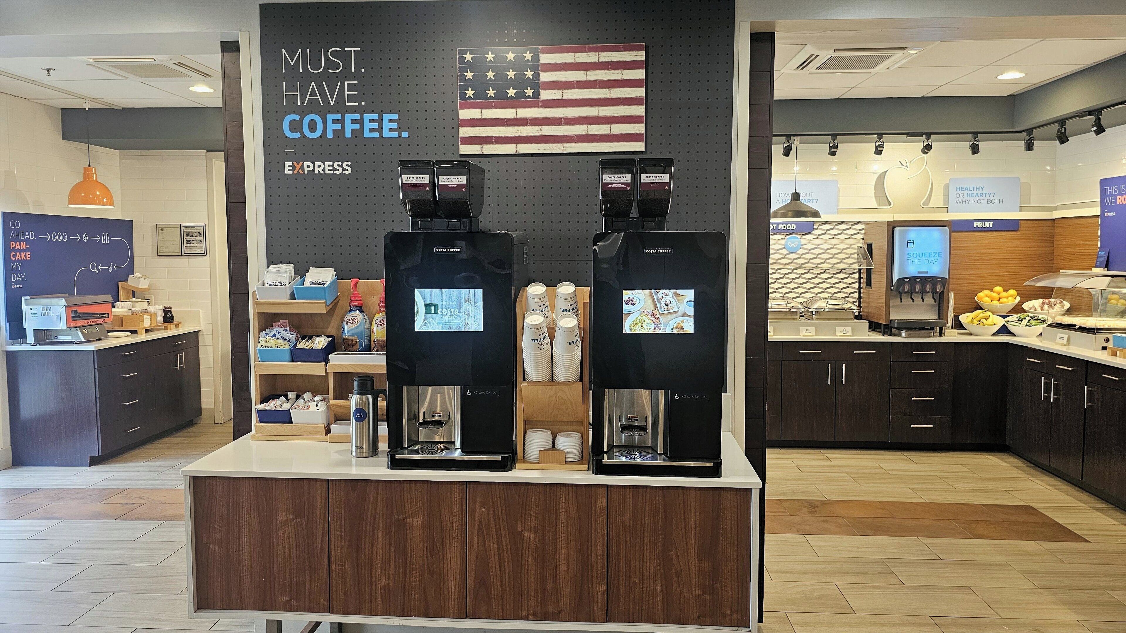 A coffee shop interior with two coffee machines, a wall with an American flag, and a menu board.