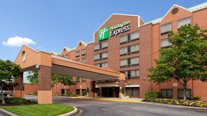 A Holiday Inn Express hotel with a brick facade, a covered entrance, and a landscaped area with flowers and trees.