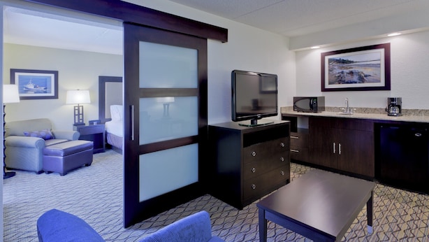 A hotel room with a sofa, a small table, a TV, a microwave, a coffee maker, and a painting on the wall.