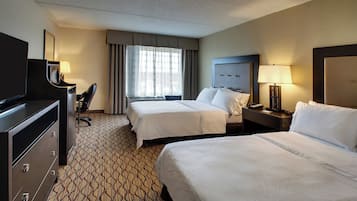 A hotel room with two beds, a desk, a chair, a television, and a window with curtains.