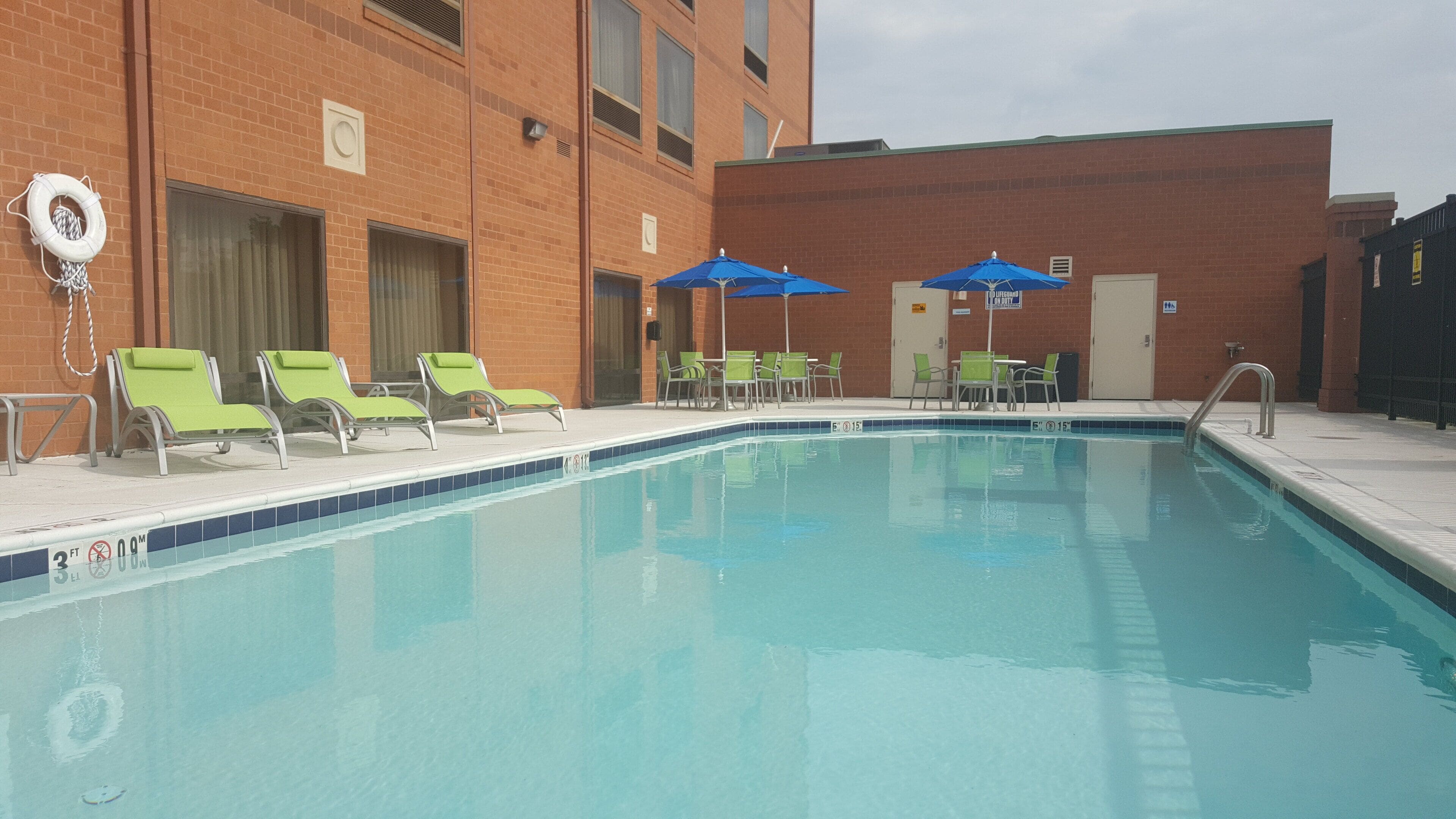 Una piscina con sillas de descanso y sombrillas, rodeada por un edificio de ladrillo.