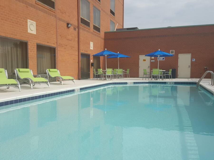 A swimming pool with lounge chairs and umbrellas, surrounded by a brick building.