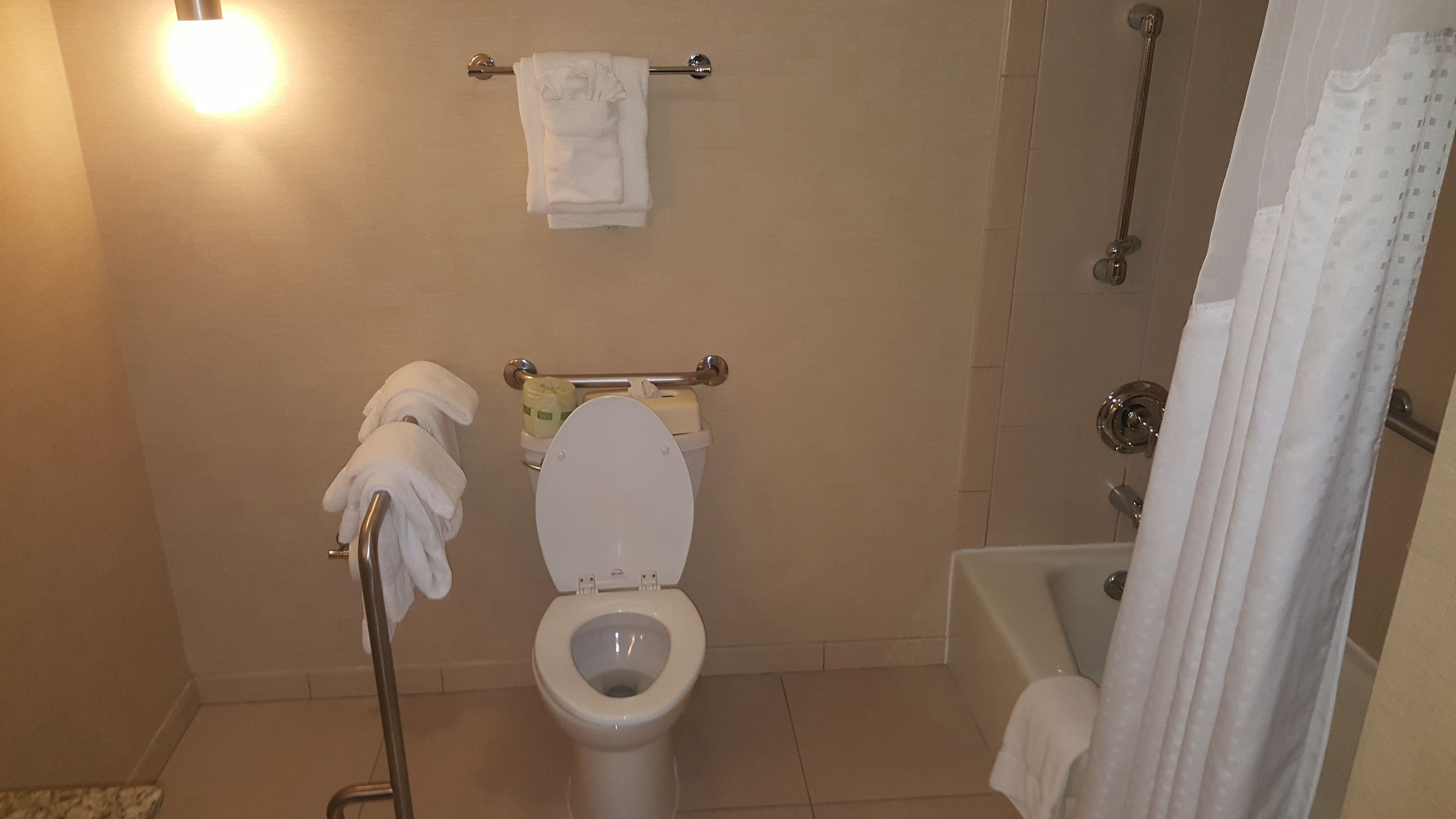 Casa de banho com sanita, um porta-toalhas com toalhas, cortina de chuveiro e rolo de papel higiénico.