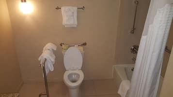 Casa de banho com sanita, um porta-toalhas com toalhas, cortina de chuveiro e rolo de papel higiénico.