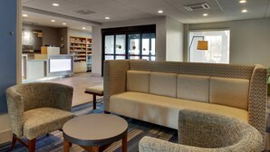 A lobby with a sofa, armchairs, a small table, a kitchen area, and a bookshelf.