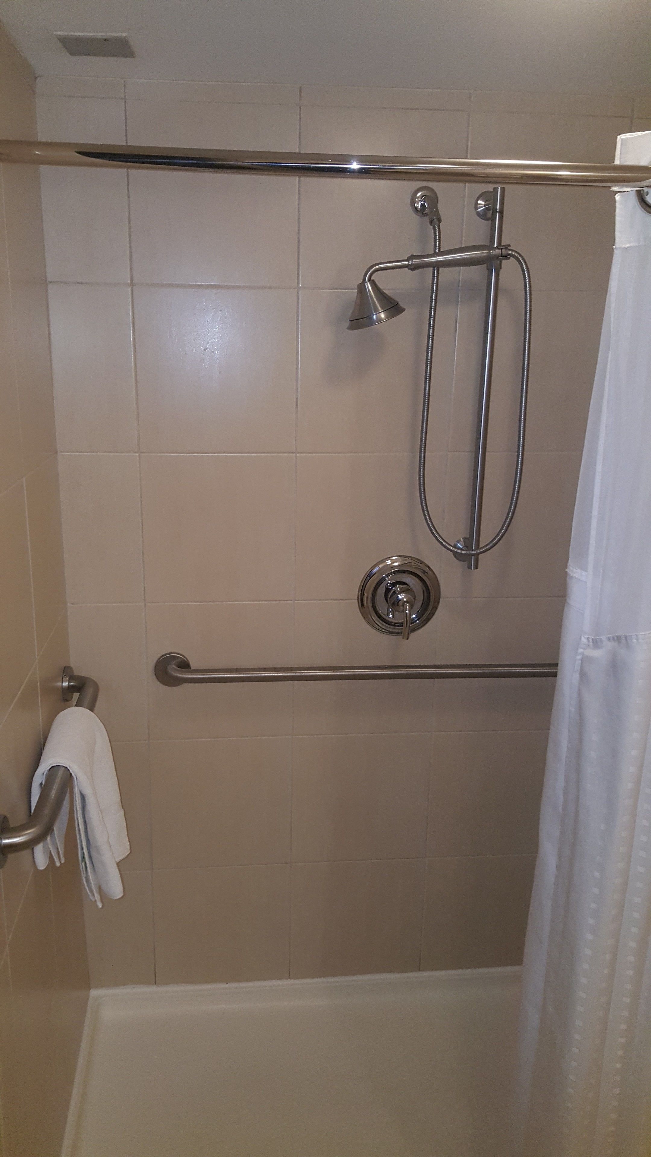 A shower area with a grab bar, a handheld showerhead, and a curtain.