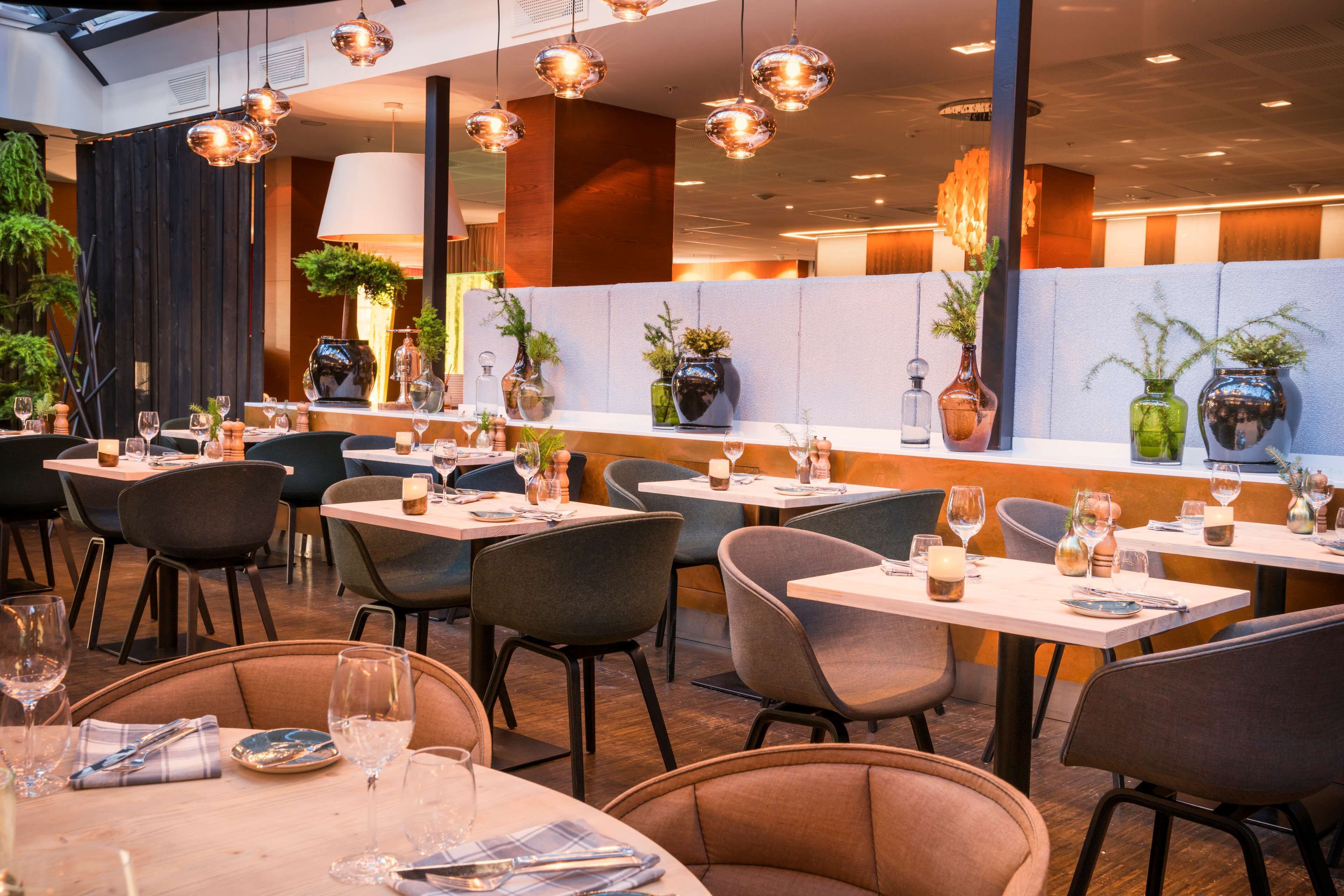 En modern restaurang med flera bord, stolar och hängande taklampor.