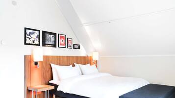 Una habitación de hotel moderna con cabecera de madera, cama con ropa blanca, una mesita con lámpara y un banco.
