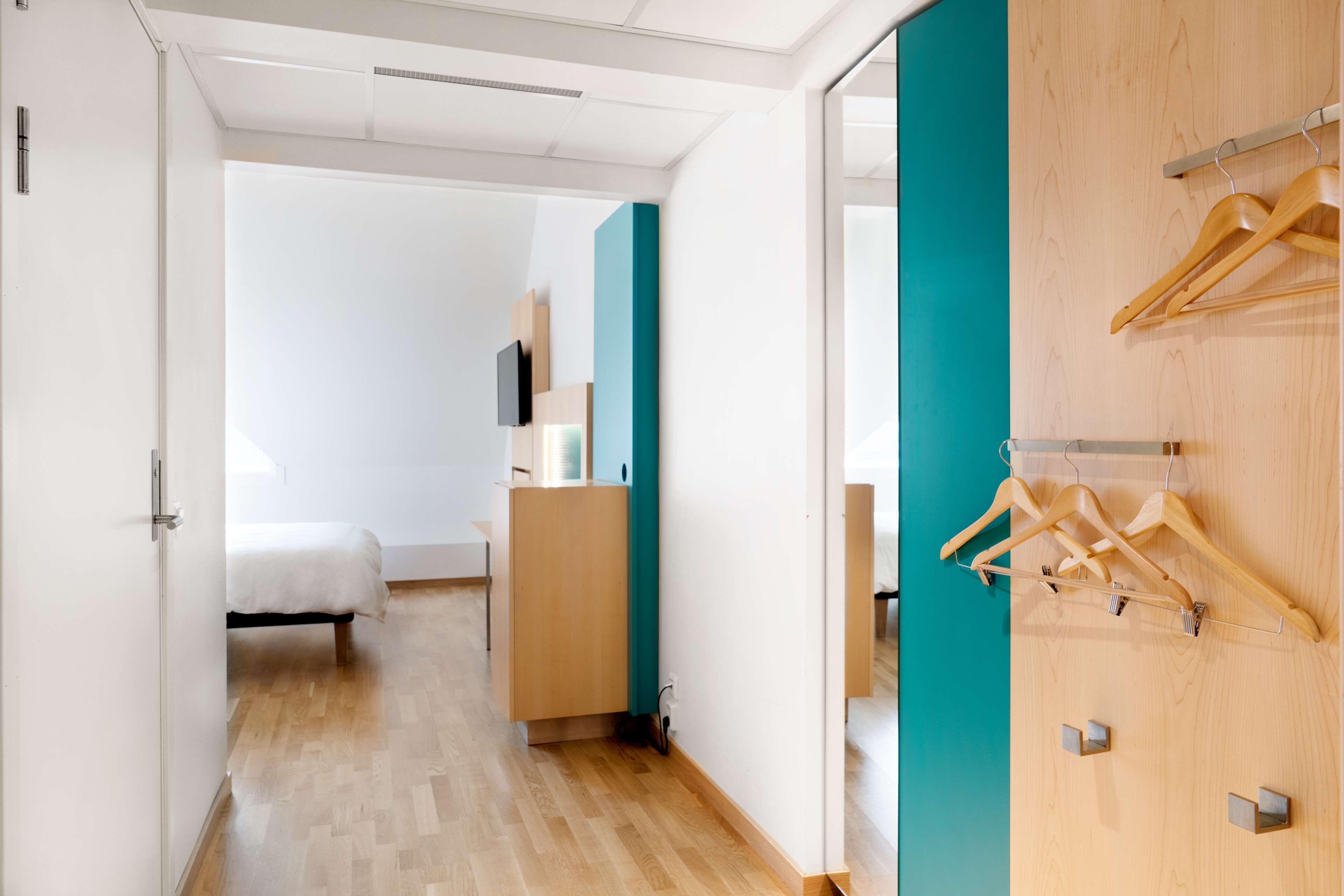 Ein modernes Hotelzimmer mit Holzboden, einem Bett, einem Schreibtisch und einem Kleiderschrank mit Holzaufhängern.