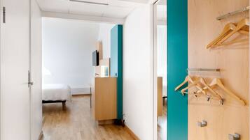Ein modernes Hotelzimmer mit Holzboden, einem Bett, einem Schreibtisch und einem Kleiderschrank mit Holzaufhängern.