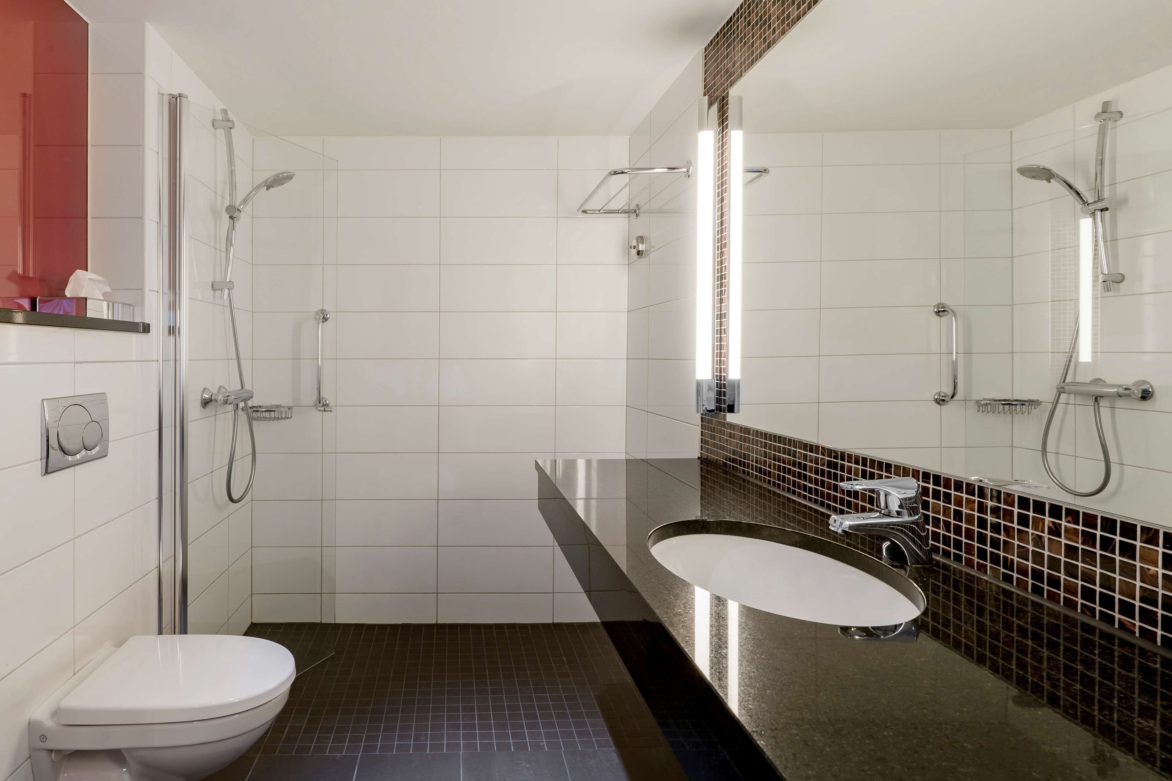 A modern bathroom with a white toilet, a glass-enclosed shower, a vanity with a mirror, and a black-tiled floor.