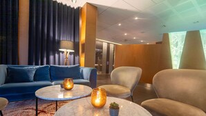 A modern lobby with a blue sofa, two round marble tables with candles, a grey armchair, and a wooden accent wall.