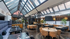 En moderne restaurant med høje lofter, glasfacader og forskellige siddepladser, inklusiv borde og båse.