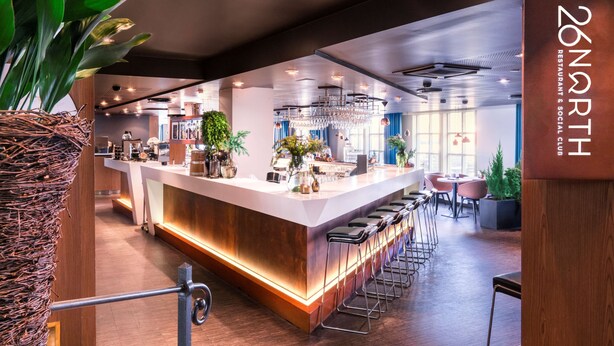 Et moderne barområde med disk, barstole og et skilt der står "26 NORTH RESTAURANT & SOCIAL CLUB".
