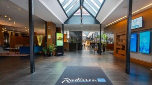 En moderne hotellobby med ovenlys, siddeområde og Radisson-logo på gulvet.