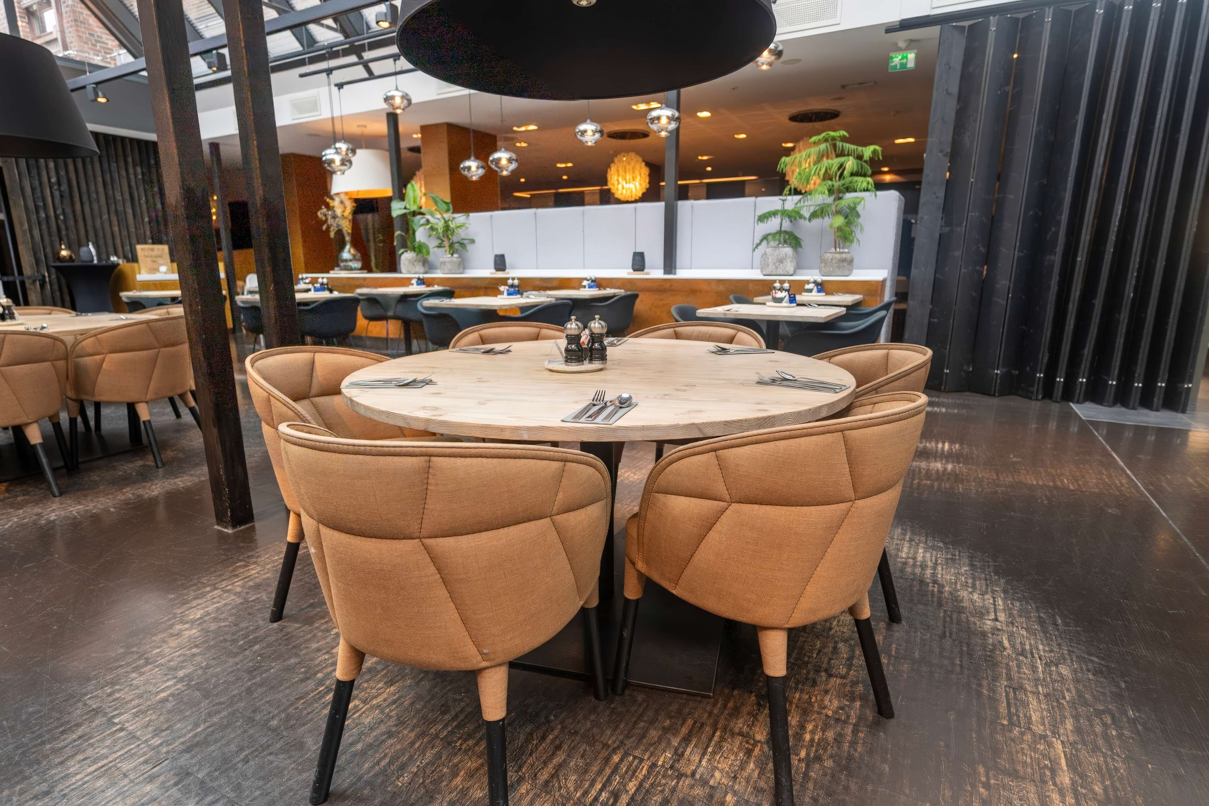 Interior moderno de restaurante con mesas redondas, sillas con reposacabezas de color marrón y piso de madera oscura.