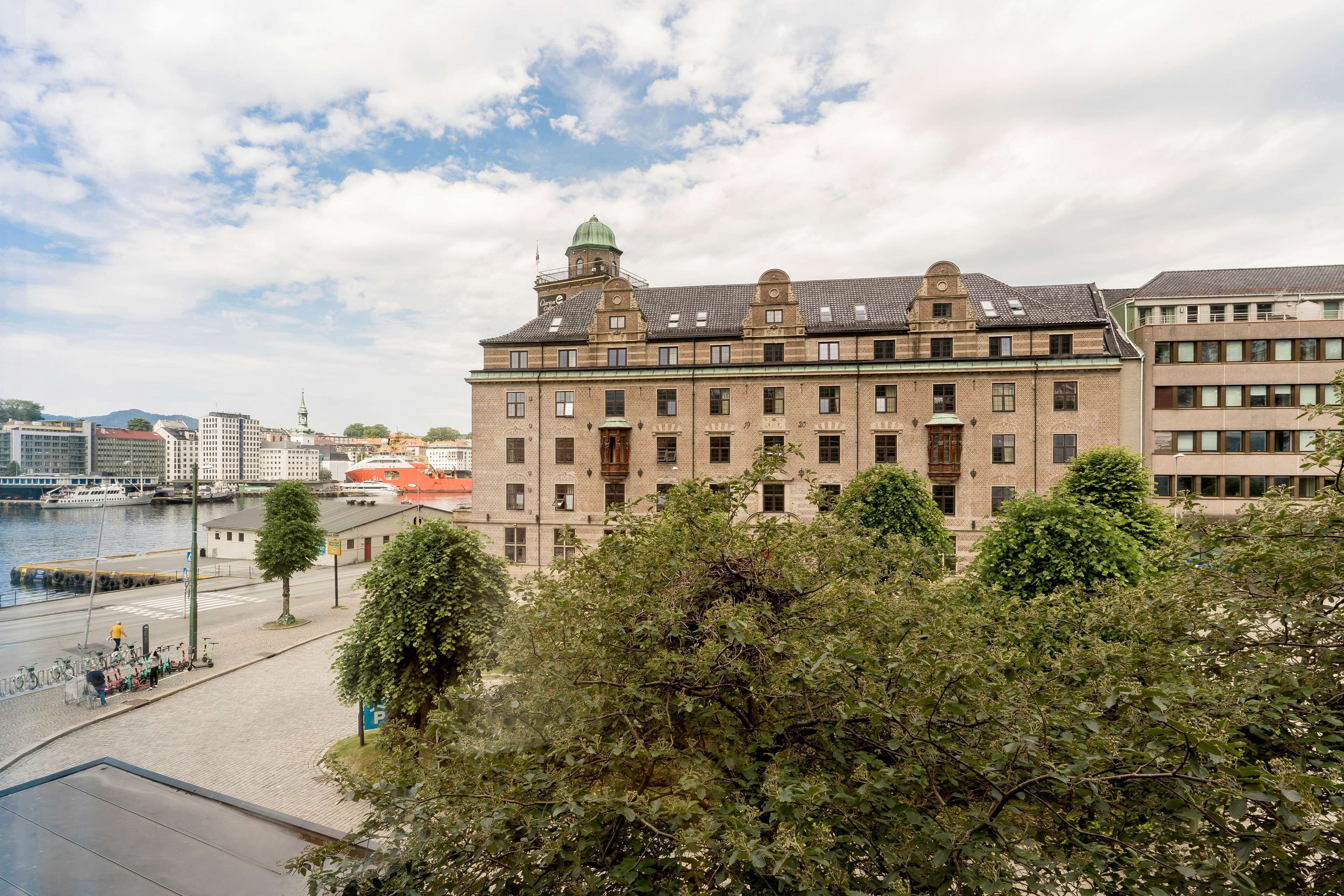 Un bâtiment historique doté d’une tour imposante et de nombreuses fenêtres, situé au bord de l’eau, avec des arbres en premier plan.
