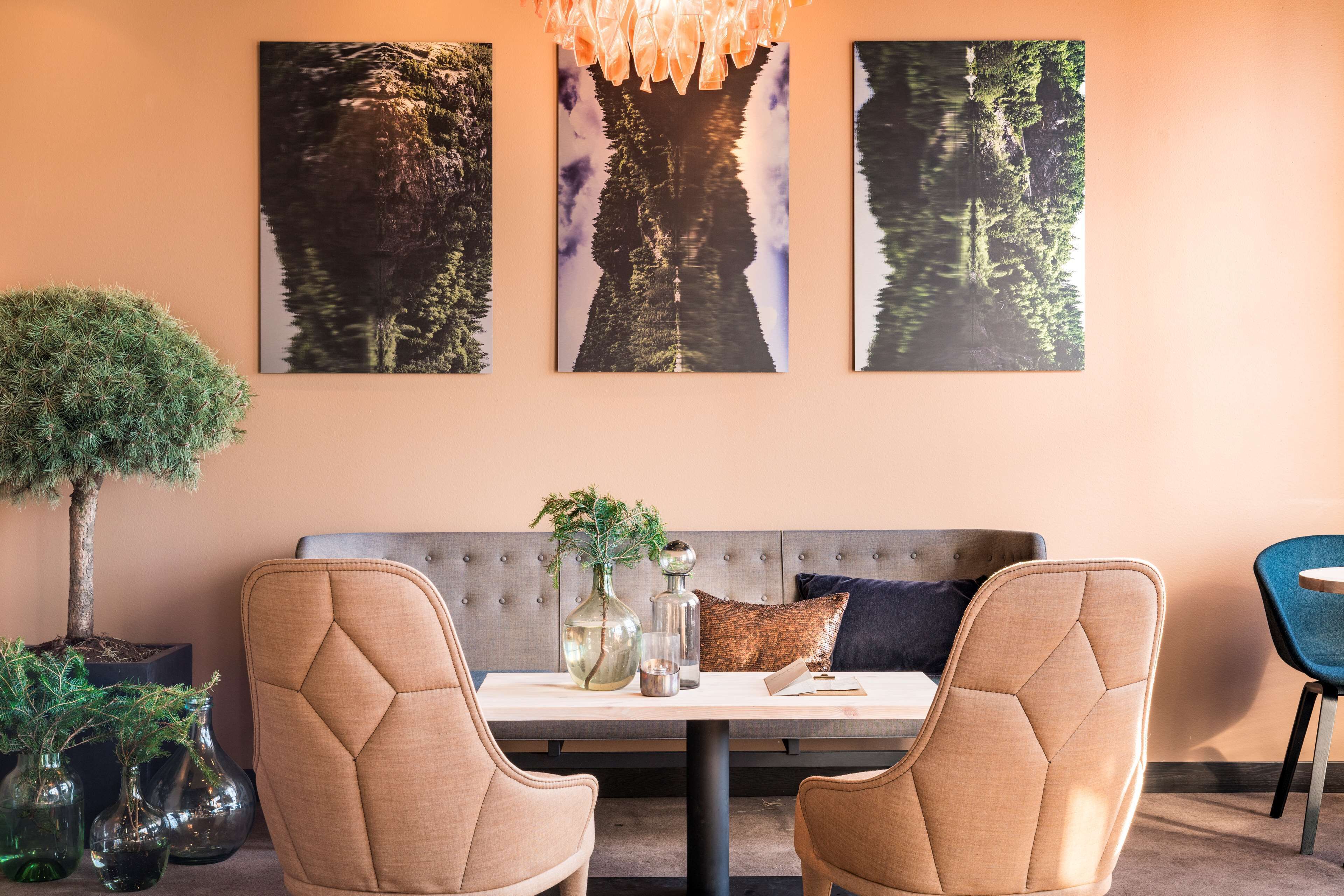 A modern dining area with a cushioned bench, two upholstered chairs, a table with a vase and glass, and three framed nature photographs on the wall.