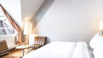 A modern hotel room with a bed, a chair, a small table, and a lamp.