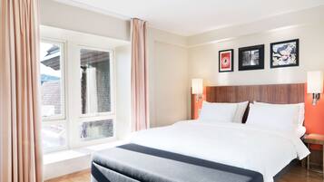 A hotel room with a large bed, a window with curtains, a wooden headboard, and three framed pictures on the wall.