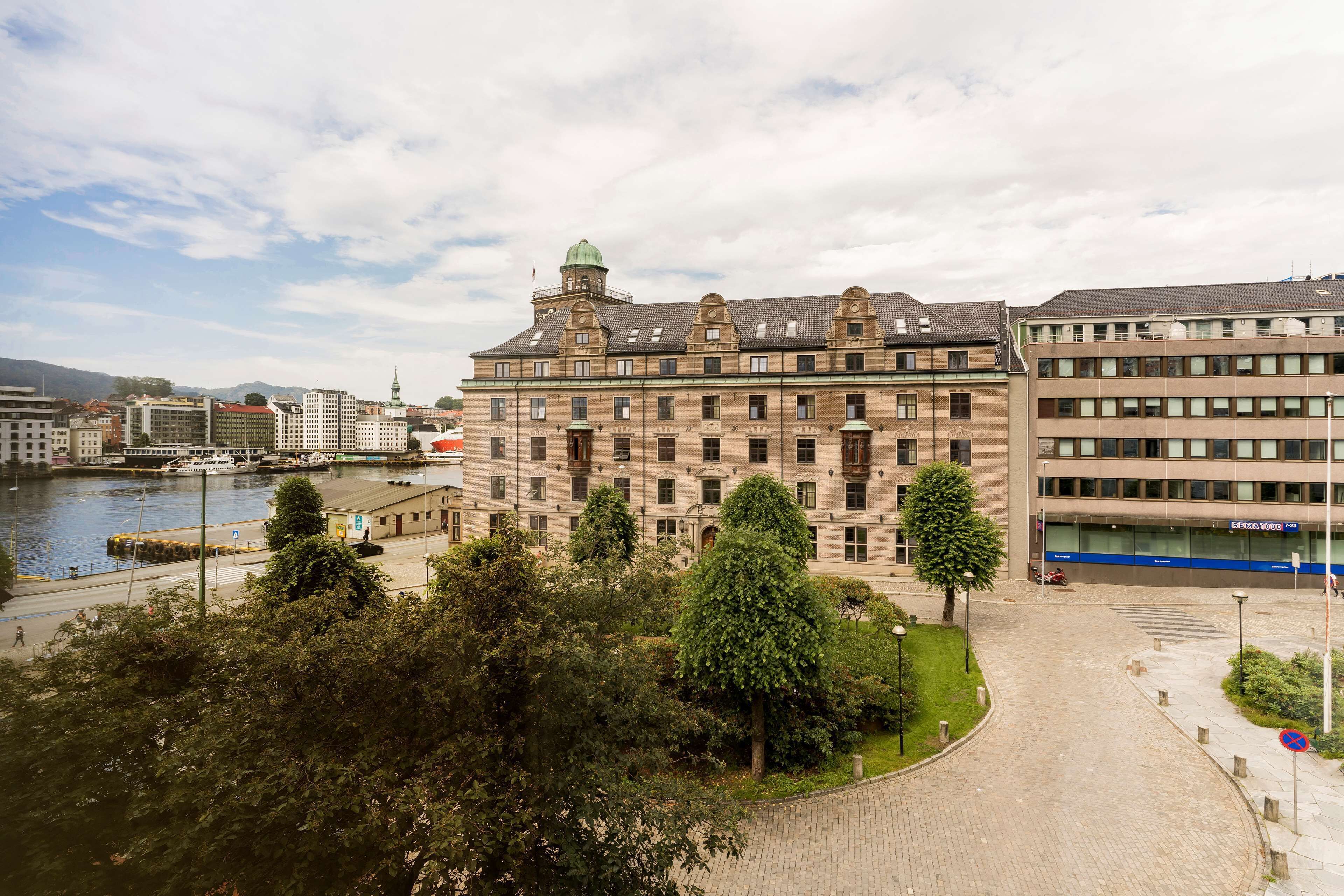 A historic building with a central tower, surrounded by trees and a paved area.