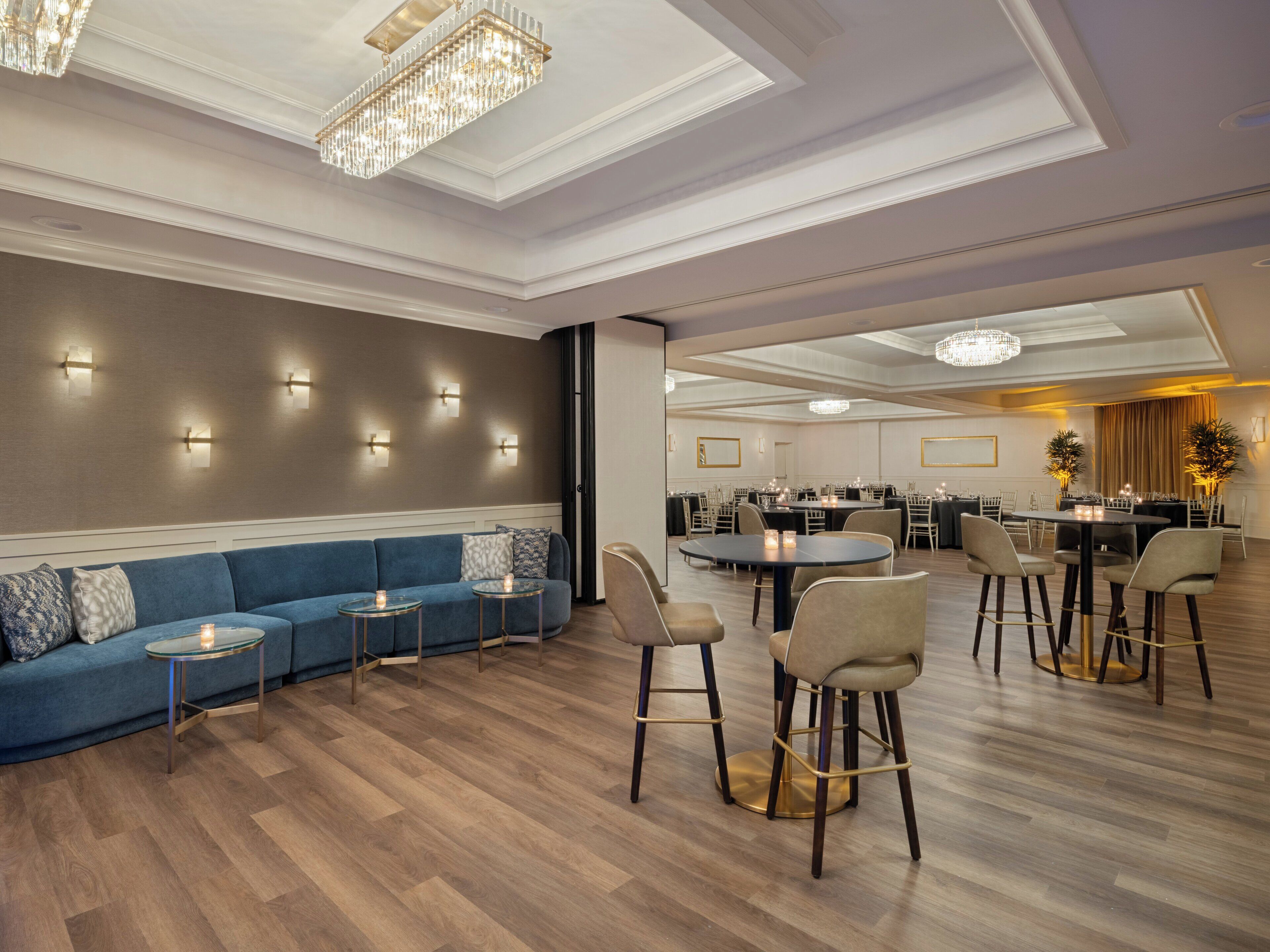 A modern hotel lobby with a blue sofa, round tables, and bar stools.