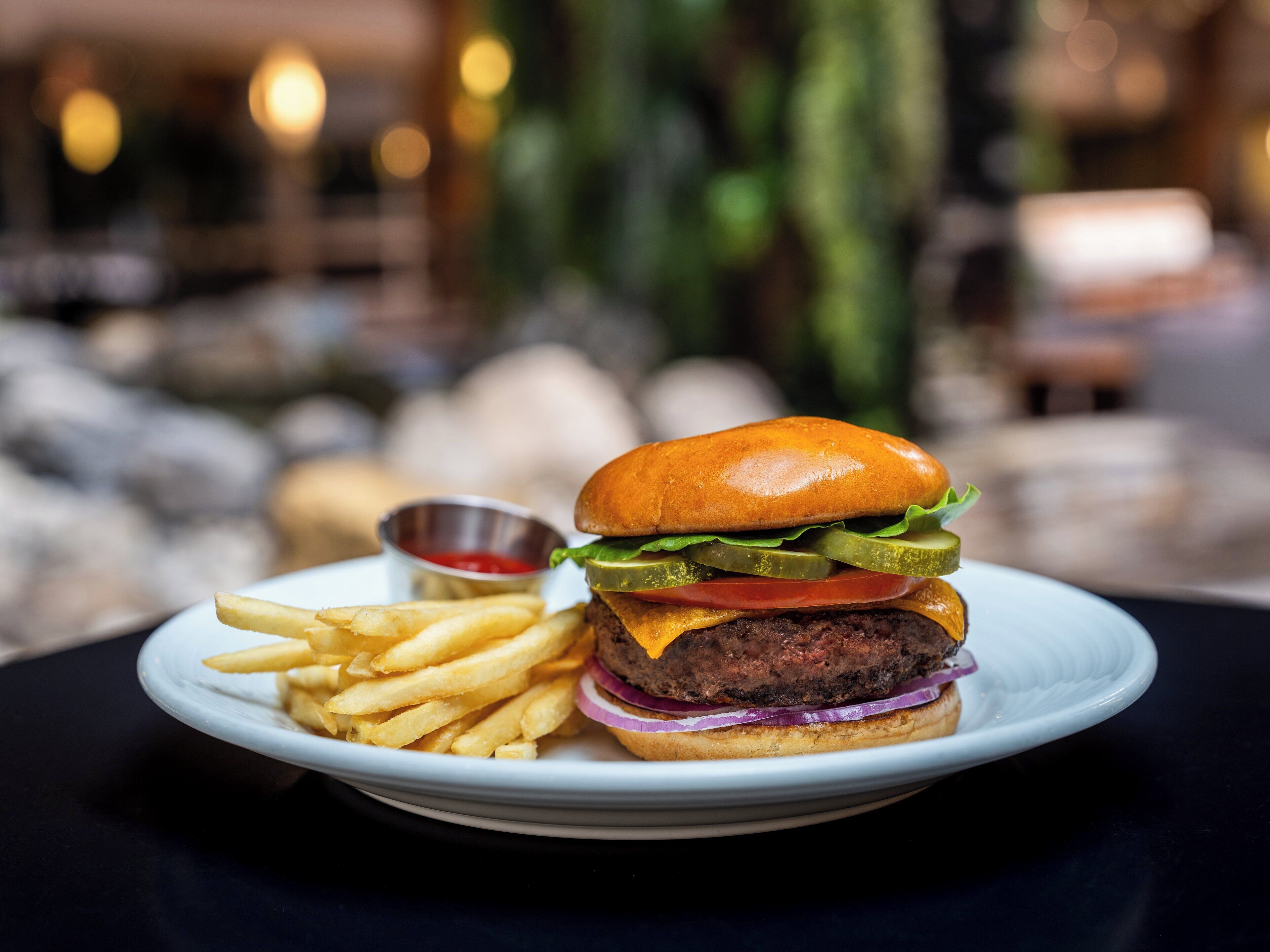 A plate with a burger, fries, and a small container of ketchup.