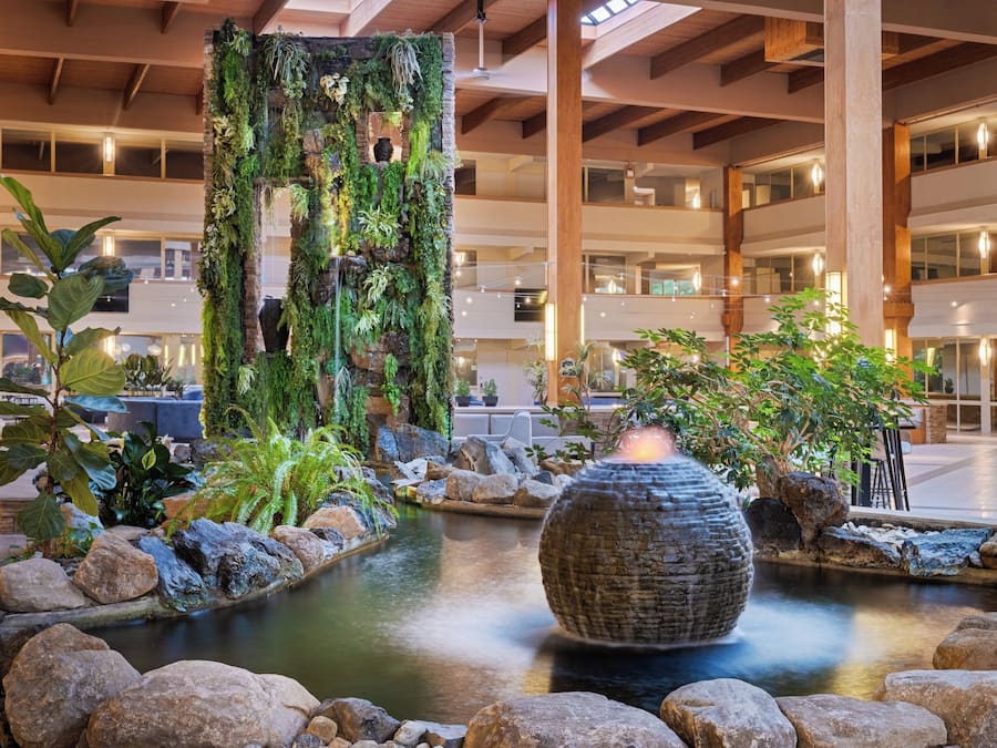 A lobby with a central water feature, a stone wall with greenery, and a modern interior design.