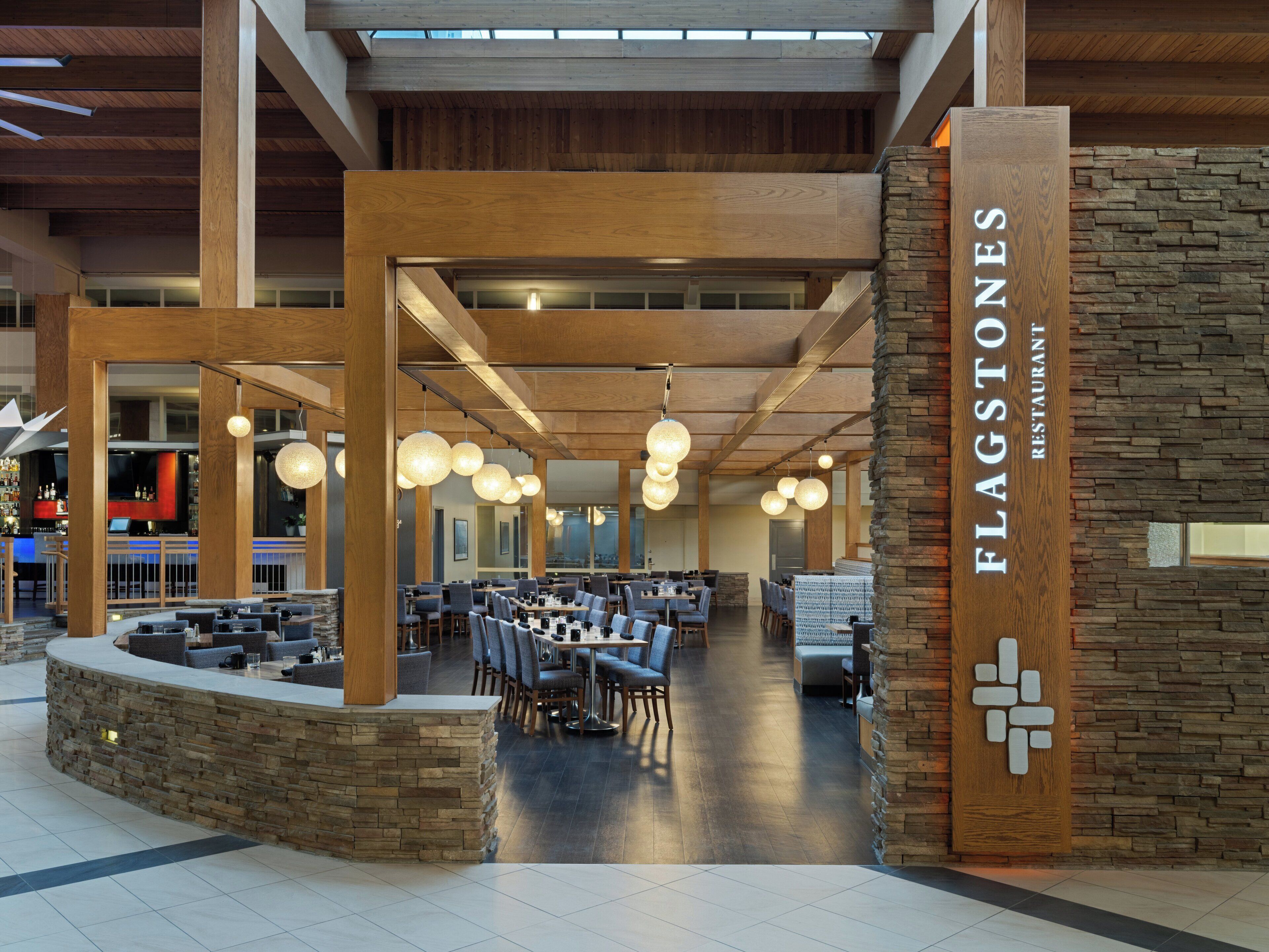A spacious restaurant interior with high wooden beams, stone accents, and modern pendant lighting.